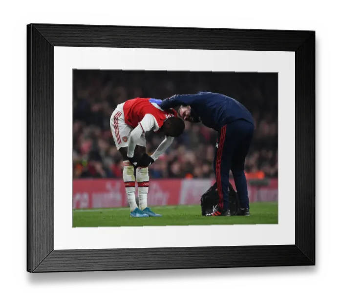Framed Print : Arsenal's Nicolas Pepe Receives Treatment from Physio during Arsenal v Manchester United (2019-20)
