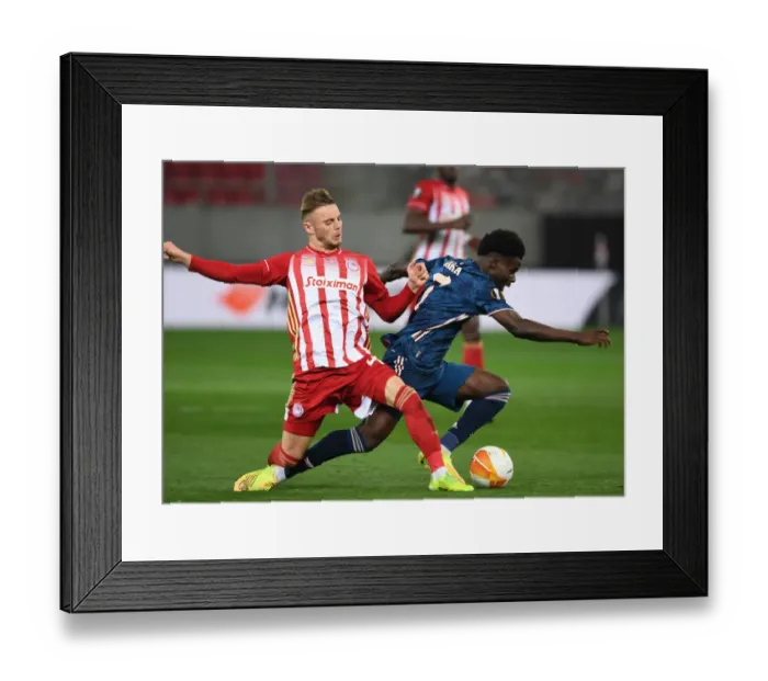 Framed Print : Bukayo Saka Faces Off Against Oleg Reabciuk in Empty Karaiskakis Stadium: Olympiacos vs. Arsenal, UEFA Europa League Round of 16
