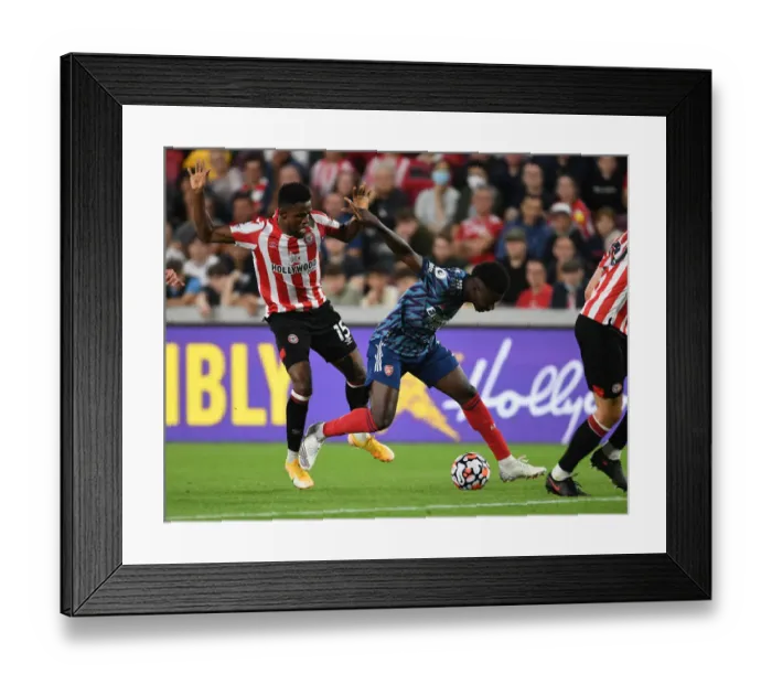 Framed Print : Bukayo Saka vs. Frank Onyeka: Intense Battle at Brentford Community Stadium - Arsenal vs. Brentford, Premier League 2021-22