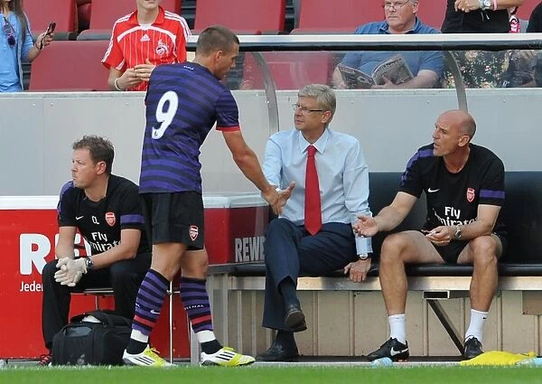 Arsene Wenger the Arsenal Manager shakes hands with Lukas Podolski as he comes of the pitch