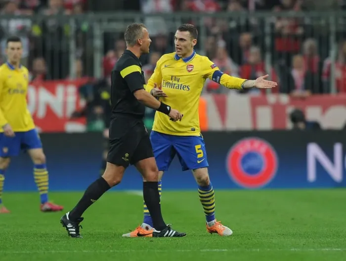 Framed Print : Thomas Vermaelen Confronts Referee Svein Oddvar Moen in Tense Arsenal-Bayern Clash