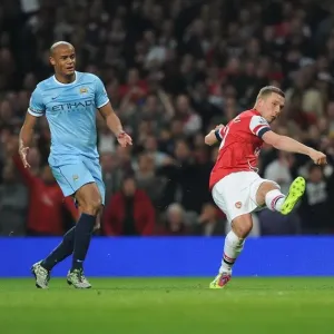 Arsenal's Lukas Podolski Outmaneuvers Manchester City's Vincent Kompany in the 2013/14 Premier League Clash