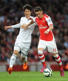 Arsenal Swansea City 2014/15 Collection: Mesut Ozil vs. Ki Sung-Yueng: A Premier League Battle at Emirates Stadium (2014/15)