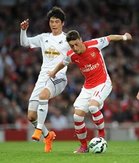 Arsenal Swansea City 2014/15 Collection: Mesut Ozil vs. Ki Sung-Yueng: A Premier League Battle at Emirates Stadium, 2015