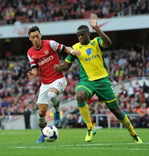 Arsenal V Norwich City 2013-14 Prints: Mesut Ozil vs Sebastien Bassong: A Football Rivalry Unfolds at Arsenal vs Norwich City